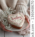 A woman holds a heart-shaped cake with the word "Baby" written on it.  136048670