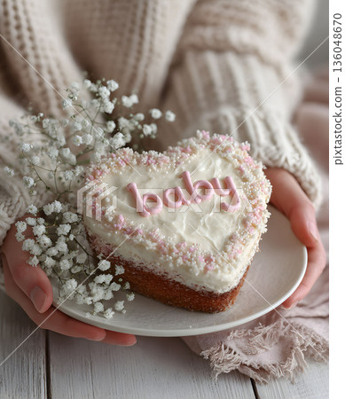 A woman holds a heart-shaped cake with the word "Baby" written on it.  136048670