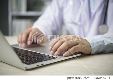 Doctor types on laptop in clinic office for EMR EHR patient record update telemedicine telehealth healthcare communication data entry workflow productivity modern hospital concept. Doctor types on laptop in clinic office for EMR EHR patient record update telemedicine telehealth healthcare communication data entry workflow productivity modern hospital concept. 136048781