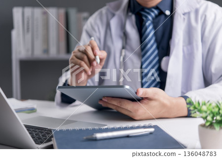 Doctor uses tablet with stylus in clinic office for medical record ehealth telemedicine patient management healthcare technology workflow data entry modern hospital concept. Doctor uses tablet with stylus in clinic office for medical record ehealth telemedicine patient management healthcare technology workflow data entry modern hospital concept. 136048783