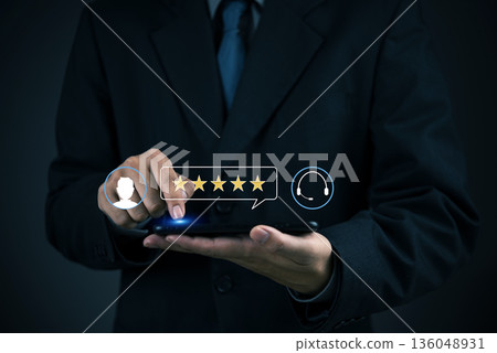 Feedback, CSAT Person in suit selects five stars on mobile at work to evaluate service experience, emphasizing positive testimonial, loyalty, and customer experience concept. 136048931