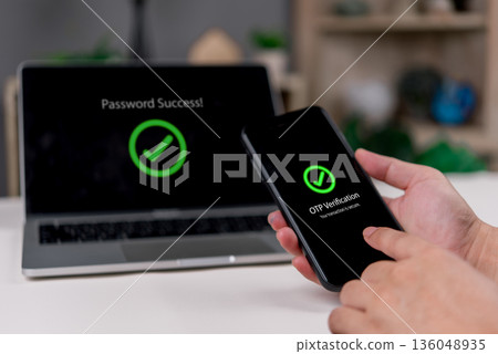 Security Password , Hands confirm OTP on a smartphone while the laptop shows success in a clean workspace to finish login, 2FA, smartphone mobile authentication, and identity protection concept. 136048935