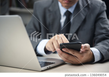 businessman uses a smartphone, laptop computer at an office desk to manage online communication, schedule meetings, and boost productivity. concept mobile digital workflow. businessman uses a smartphone, laptop computer at an office desk to manage online communication, schedule meetings, and boost productivity. concept mobile digital workflow. 136049054