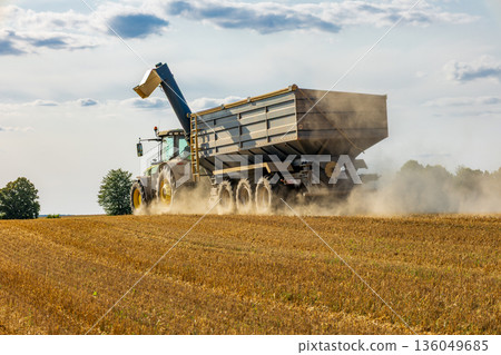 A massive combine harvester skillfully collects crops in a golden field, sending dust into the air under a clear blue sky A massive combine harvester skillfully collects crops in a golden field, sending dust into the air under a clear blue sky 136049685
