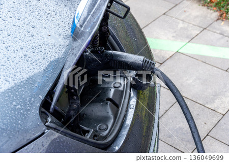 A rain-dropped electric vehicle charges in a busy parking lot, highlighting a moment of sustainability A rain-dropped electric vehicle charges in a busy parking lot, highlighting a moment of sustainability 136049699