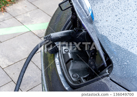 A sleek electric car is parked at a charging station, rain droplets clinging to its surface, as green lines mark the parking area A sleek electric car is parked at a charging station, rain droplets clinging to its surface, as green lines mark the parking area 136049700