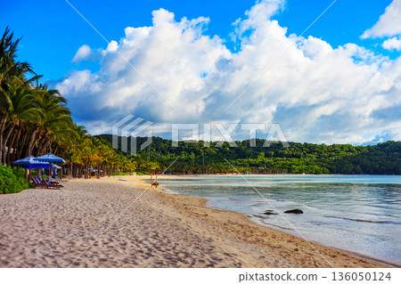 A beach with a blue umbrella and a few chairs 136050124