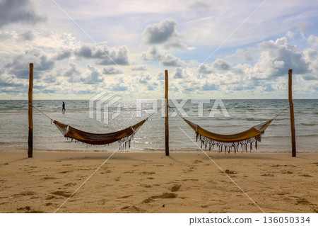 Two beach hammocks are hanging from two wooden posts on a beach Two beach hammocks are hanging from two wooden posts on a beach 136050334