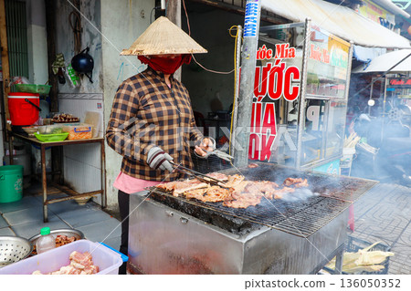 Iceland Phu Quoc Vietnam 5.7.2025. A woman wearing a mask is cooking meat on a grill 136050352