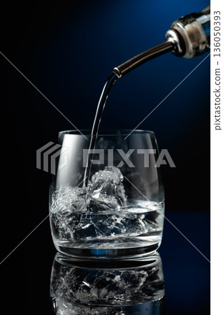 Crystal clear vodka being poured over ice in a glass. Crystal clear vodka being poured over ice in a glass. 136050393