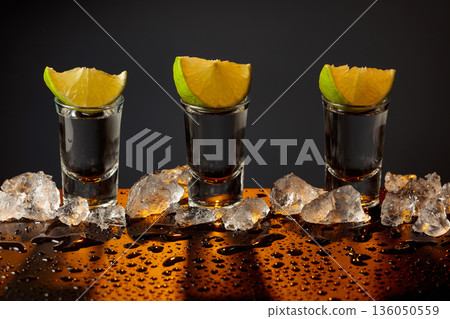 Gold tequila shots with lime slices on a wet black table. Gold tequila shots with lime slices on a wet black table. 136050559