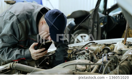 Professional automotive technician documenting engine repair, photographing vehicle components using smartphone while standing in workshop Professional automotive technician documenting engine repair, photographing vehicle components using smartphone while standing in workshop 136051020