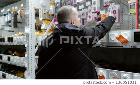 Skilled electrician reviewing light switches and electrical fixtures in hardware store, comparing options for professional home improvement and electrical upgrade work 136051031