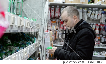 Electrician carefully reviewing light switch packaging in hardware store, surrounded by electrical supplies, tools scattered nearby on shelves 136051035