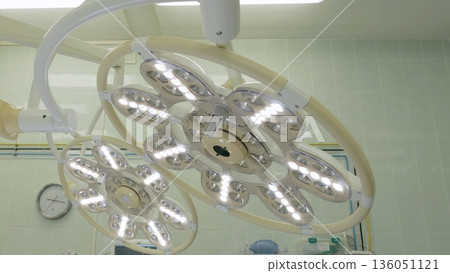 Russia Tomsk 05.07.2025: Closeup modern surgical lights illuminating operating theater, circular LED array casting uniform brightness, ceiling mount and control mechanisms visible, sterile Russia Tomsk 05.07.2025: Closeup modern surgical lights illuminating operating theater, circular LED array casting uniform brightness, ceiling mount and control mechanisms visible, sterile 136051121