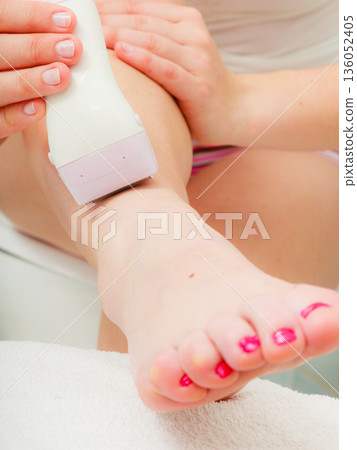 Woman shaving legs with depilator in bathroom Woman shaving legs with depilator in bathroom 136052405