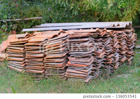 Ceramic roofing tiles stacked in yard. Pile of terracotta colored tiles. Traditional building material. Roof tiles. 136053541