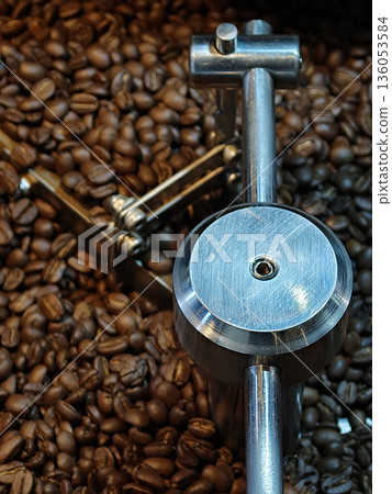 Freshly roasted coffee beans surround metallic coffee roasting machine, showcasing intricate design and craftsmanship involved coffee preparation. rich aroma of coffee fills air, inviting Freshly roasted coffee beans surround metallic coffee roasting machine, showcasing intricate design and craftsmanship involved coffee preparation. rich aroma of coffee fills air, inviting 136053584