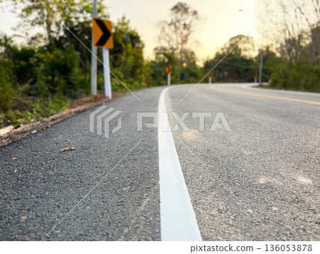 a curved asphalt road with a white edge line and warning signs, surrounded by trees at sunset, symbolizing direction, decision making, caution, journey, change, and future path a curved asphalt road with a white edge line and warning signs, surrounded by trees at sunset, symbolizing direction, decision making, caution, journey, change, and future path 136053878