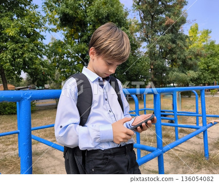 Young Boy using phone. A schoolboy uses his phone in the schoolyard 136054082
