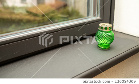 Green glass candle holder on window sill with blurred outdoor view 136054309