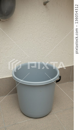 Empty gray plastic bucket on tiled floor for cleaning or storage Empty gray plastic bucket on tiled floor for cleaning or storage 136054312