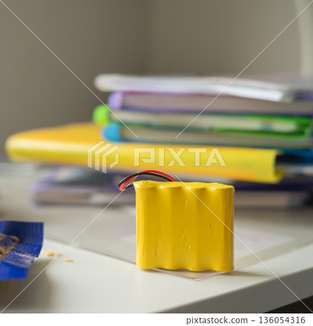 Yellow battery pack on desk with stacked books in background Yellow battery pack on desk with stacked books in background 136054316
