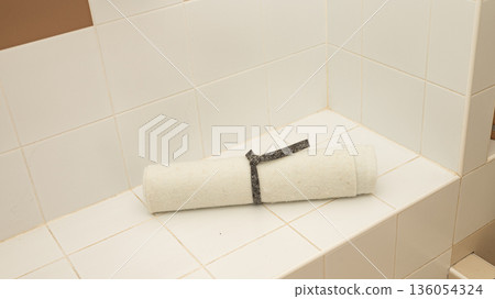White rolled towel on a tiled bathroom shelf with brown wall White rolled towel on a tiled bathroom shelf with brown wall 136054324