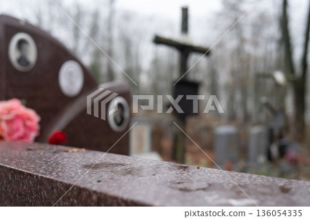Wet cemetery scenes with tombstones and cross on overcast day 136054335