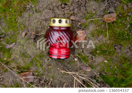Red glass remembrance candle on mossy ground with fallen leaves 136054337