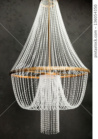 Elegant beaded chandelier with brass frame against dark backdrop 136054350