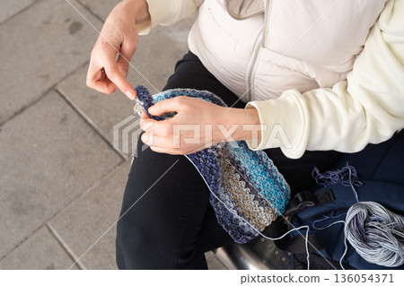 I Love Yarn Day. Young caucasian female knitting blue patterned scarf outdoor 136054371