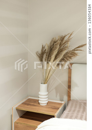 Minimalist bedroom corner with pampas grass in white vase on wooden nightstand Minimalist bedroom corner with pampas grass in white vase on wooden nightstand 136054384