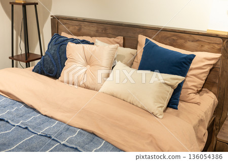 Cozy bedroom with wooden headboard and plush pillows in warm tones Cozy bedroom with wooden headboard and plush pillows in warm tones 136054386