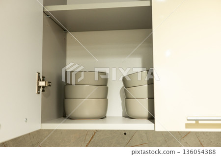 Stacked ceramic bowls in open kitchen cabinet with light cream interior 136054388