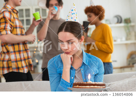 Sad lonely frustrated unhappy young woman looking at birthday cake with candle on birthday party. Girl sad disappointed thinking about life. Birthday party with friends. People celebrating birthday Sad lonely frustrated unhappy young woman looking at birthday cake with candle on birthday party. Girl sad disappointed thinking about life. Birthday party with friends. People celebrating birthday 136054806