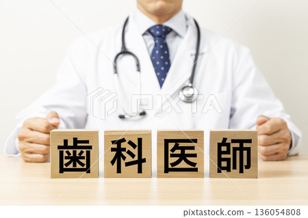 一塊寫著「牙醫」字樣的磚塊和一個醫生 一塊寫著「牙醫」字樣的磚塊和一個醫生 136054808