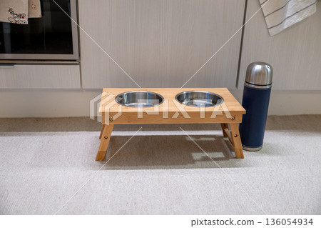 Elevated wooden pet feeding station with double bowl and thermos in modern kitchen 136054934