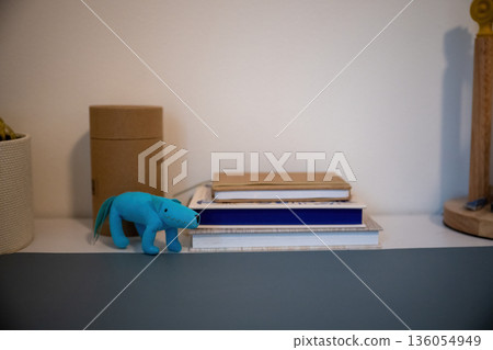 Minimal still life with blue toy dinosaur on bookshelf with notebooks and cardboard boxes in cozy home interior 136054949