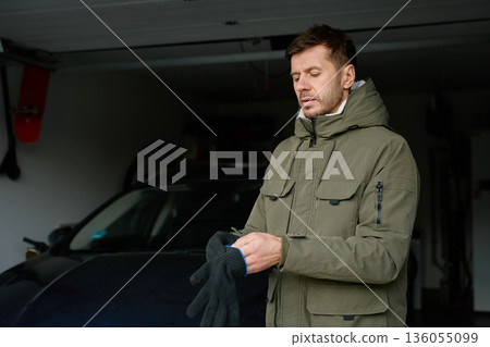 Man putting on gloves while standing inside residential garage near car Man putting on gloves while standing inside residential garage near car 136055099