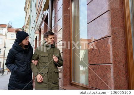 Man and woman walking together and looking at shop window on city street 136055100