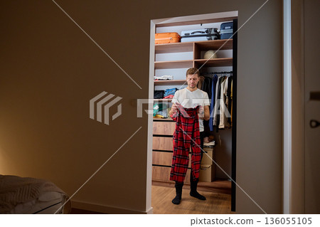 Man standing in walk in closet and holding clothes while choosing outfit Man standing in walk in closet and holding clothes while choosing outfit 136055105