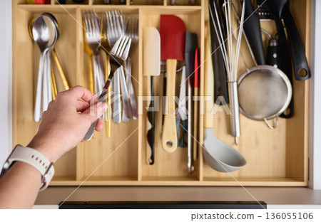 Hand placing metal fork into wooden organizer tray inside kitchen drawer Hand placing metal fork into wooden organizer tray inside kitchen drawer 136055106