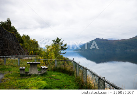 Scenic lakeside picnic area with mountain reflection in calm Norway fjord 136055107