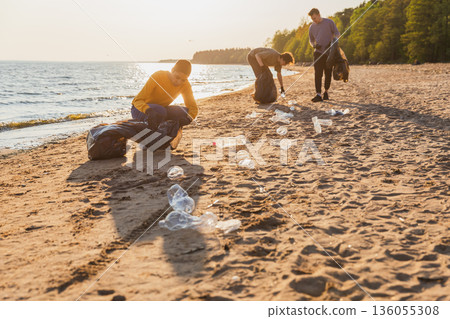 Earth day. Volunteers activists team collects garbage cleaning of beach coastal zone. Woman mans puts plastic trash in garbage bag on ocean shore. Environmental conservation coastal zone cleaning 136055308