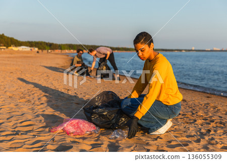 Earth day. Volunteers activists team collects garbage cleaning of beach coastal zone. Woman mans puts plastic trash in garbage bag on ocean shore. Environmental conservation coastal zone cleaning Earth day. Volunteers activists team collects garbage cleaning of beach coastal zone. Woman mans puts plastic trash in garbage bag on ocean shore. Environmental conservation coastal zone cleaning 136055309