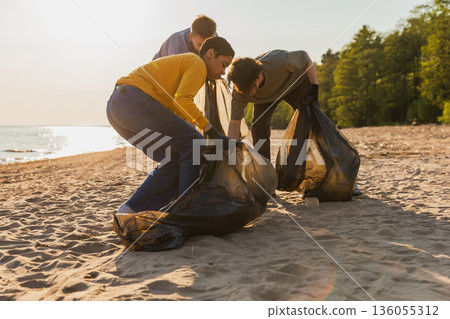 Earth day. Volunteers activists collects garbage cleaning of beach coastal zone. Woman and mans puts plastic trash in garbage bag on ocean shore. Environmental conservation coastal zone cleaning Earth day. Volunteers activists collects garbage cleaning of beach coastal zone. Woman and mans puts plastic trash in garbage bag on ocean shore. Environmental conservation coastal zone cleaning 136055312
