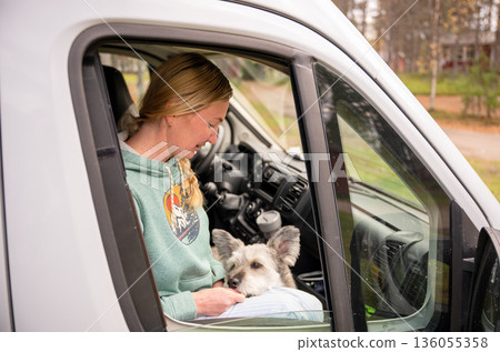 Woman traveling in camper van with dog looking through window enjoying road trip lifestyle Woman traveling in camper van with dog looking through window enjoying road trip lifestyle 136055358
