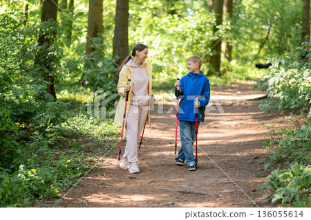 Woman and her 11-year-old son enjoying Nordic trekking walking on a sunny forest trail, embracing outdoor fitness and family time Woman and her 11-year-old son enjoying Nordic trekking walking on a sunny forest trail, embracing outdoor fitness and family time 136055614