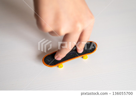 children's hands playing with toy fingerboard with yellow wheels on white background, selective focus 136055700